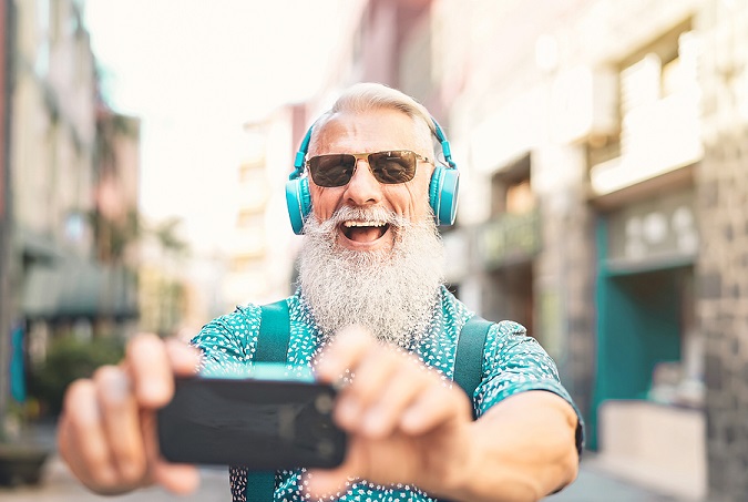 Smiling senior man with sunglasses and matching brightly colored clothes and headphones taking a selfie