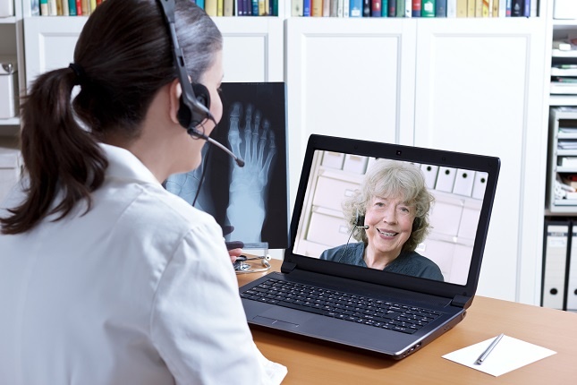 Woman with a headset seated in front of a laptop and communicating with another woman pictured on the screen