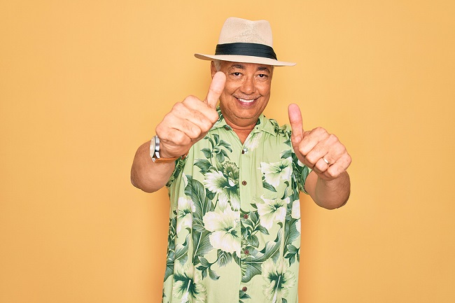 Smiling senior man wearing a Hawaiian shirt and hat and giving two thumbs up