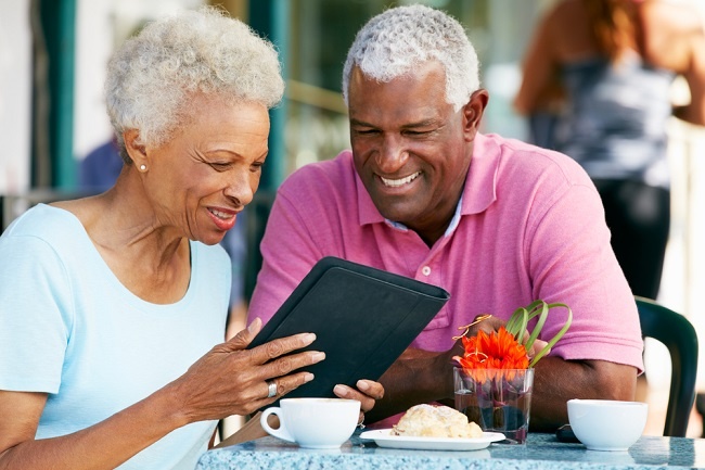 Senior couple at outdoor restaurant looking at an electronic tablet and smiling.